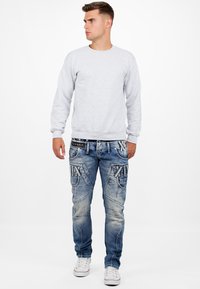 Sweatshirt en coton gris à manches longues associé à un jean en denim bleu avec des accents texturés et plusieurs poches. Baskets blanches.
