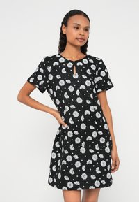 Čierne šaty s krátkymi rukávmi, majú okrúhly výstrih s kľúčovým otvorom a kvetinový vzor v bielej farbe. Vyrobené z textúrovaného materiálu, dĺžka po kolená.