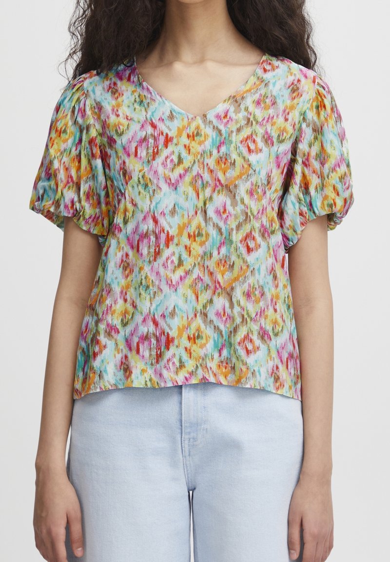 Blouse à motifs colorés avec un col en V, manches courtes bouffantes, présentant des motifs en forme de losange dans des teintes de rose, orange, turquoise et jaune.