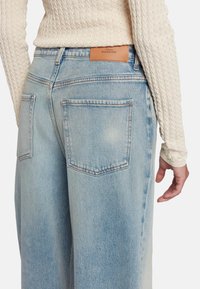 Lichtblauwe denim jeans met een hoge taille, voorzien van twee achterzakken en een leren merkpatch. De stof heeft een vervaagde afwerking.