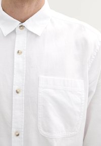 Wit overhemd met knopen, voorzien van een textiele stof, een kraag en een enkele linkerkant borstzak. De knoopdetails zijn glanzend en rond.