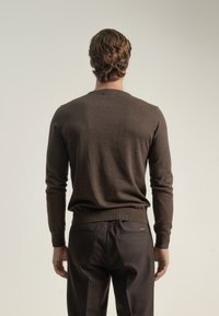 Suéter marrón de punto con mangas largas y cuello redondo, combinado con pantalones oscuros. Textura suave y diseño ajustado, con acentos mínimos.