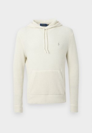 Krémovo sfarbená pletená mikina s kapucňou s textúrovaným povrchom, klokanie vrecko a sťahovacia šnúrka. Má žebrované manžety a malé logo na hrudi.