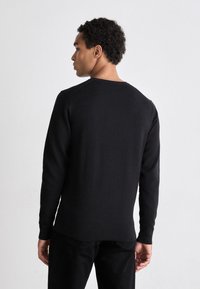 Maglione nero a maglia con un motivo testurizzato, maniche lunghe e scollo rotondo. Il design sul retro è semplice con un taglio dritto.