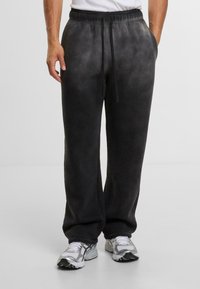 Pantalones de chándal negros con cintura elástica y cordón, que presentan una textura de degradado sutil. Bolsillos laterales visibles, corte holgado.