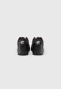 Fekete bőr Nike Air sportcipők rózsaszín részletekkel, kerek orral, párnázott bokarésszel és texturált gumitalppal. A logó a saroknál található.