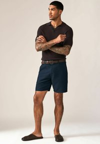 Dunkelbraunes Kurzarm-Polo, marineblaue Shorts, geflochtener brauner Gürtel und dunkelbraune Slipper. Glatte Textur, lässige Passform und klassisches Design.