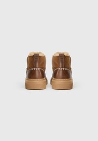 Stivali alla caviglia in pelle e suede marroni con fodera in pile beige, cuciture visibili e suole spesse in gomma, visti da dietro.