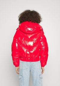 Doudoune rouge à finition brillante, avec capuche, ourlet élastique et motif en chevrons au dos. Associée à un jean cargo bleu clair.