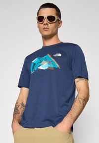Marineblauwe T-shirt met korte mouwen, voorzien van een grafisch ontwerp in turquoise en oranje. Gemaakt van een zachte stof, heeft het een ronde halslijn en een relaxte pasvorm.