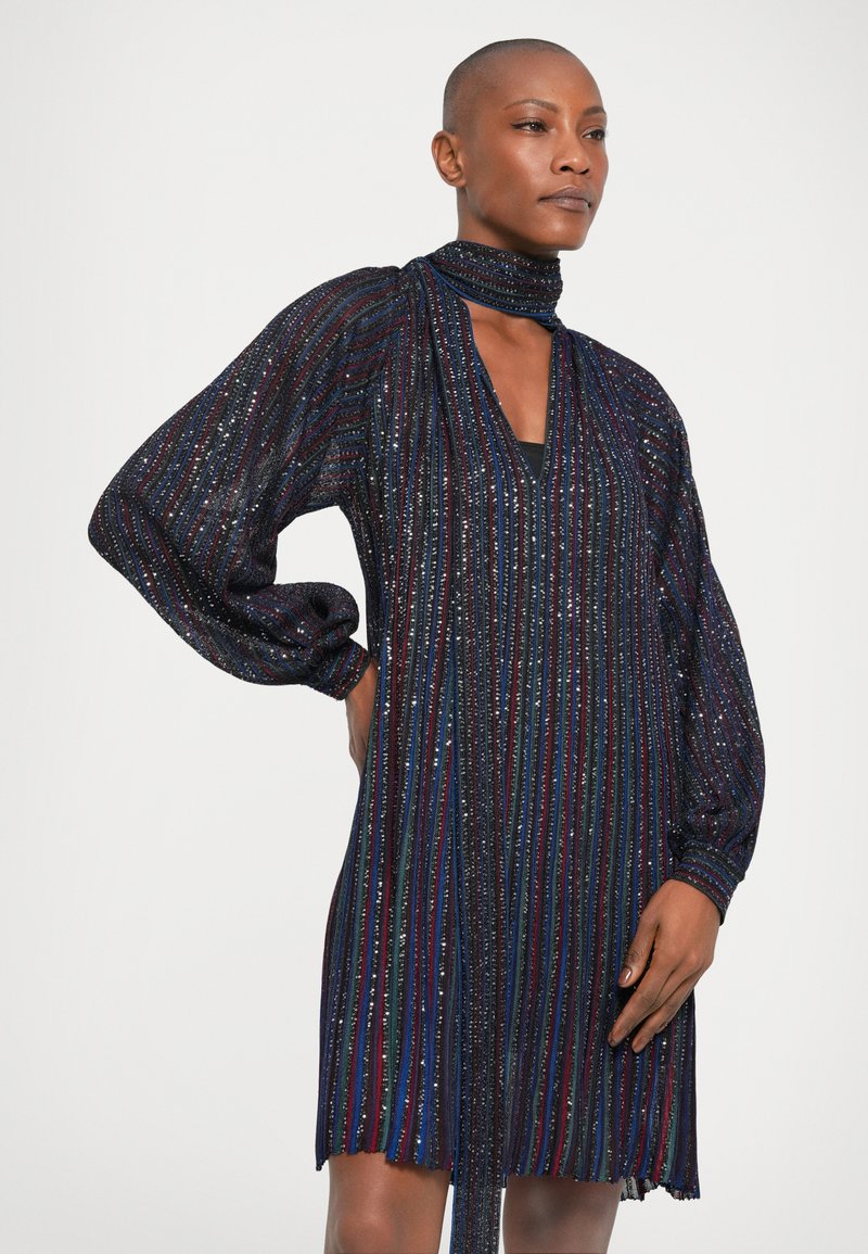 Black dress with long, puffed sleeves, featuring vertical stripes of shimmering sequins in blue, red, and silver. V-neck and tie detail at the collar.