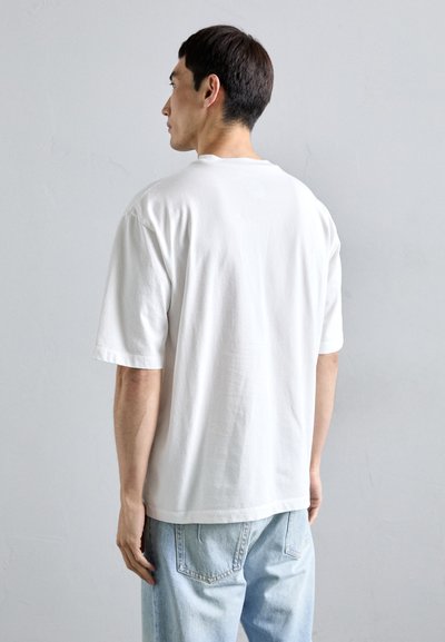 Witte katoenen t-shirt met korte mouwen, relaxte pasvorm en een ronde hals. Draag met lichtblauwe spijkerbroek, gezien vanuit de rug.