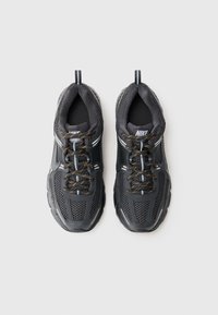 Melni Nike sporta apavi ar sieta materiālu, noapaļota purngala forma, bieza gumijas zole un apelsīnu akcenti uz šņorēm. Uz papēža un sāniem ir logos.