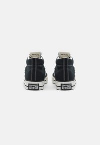 Sneakers alte nere in tela con cuciture bianche e suola in gomma testurizzata. Presentano il marchio "Converse All-Star" e "Star Player".