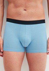 Lichtblauwe katoenen boxershorts met een zwarte tailleband met de merknaam "CALIDA." Het ontwerp heeft een contouredoek en een gladde textuur.
