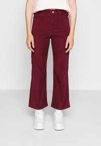 Burgundyröda vida byxor gjorda av mjuk bomull med framfickor, försedda med knapp- och dragkedjestängning, i kombination med vita sneakers.