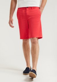 Röda bomullsshorts med rak passform, sidofickor och knappstängning, ihopparade med marinblå espadrillos. Slät textur och skräddarsydd stil.