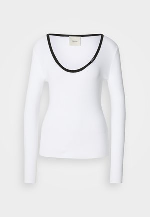 Balta garenām piedurknēm augšdaļa ar ribotu struktūru un melnu apaļu izgriezumu. Audums izskatās mīksts, gluds un pieguļošs. Zīmola etiķete redzama iekšpusē.