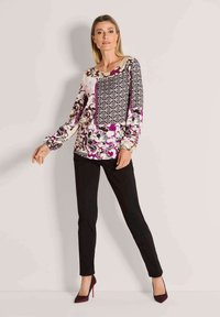 Langarmig top met bloemenpatroon in crème, bordeauxrood en zwart met een ronde hals; gecombineerd met aansluitende zwarte broek en bordeauxrode hoge hakken.