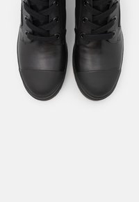 Baskets noires avec un protège orteils en cuir lisse, une tige texturée et des lacets noirs. Design minimaliste, sans logos ni motifs visibles.