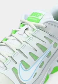 Nike edzőcipő szürke és fehér színben, zöld kiegészítőkkel. Hálós anyag, kivágott mintával. Kék swoosh logó és kerek orr.