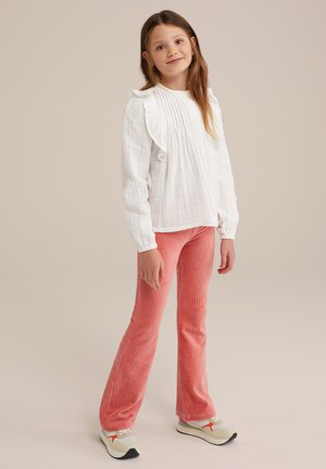 Maglietta bianca a maniche lunghe con pieghe e spalle arricciate; abbinata a pantaloni a zampa d'elefante in velluto a coste rosa; sneakers grigie e arancioni completano il look.