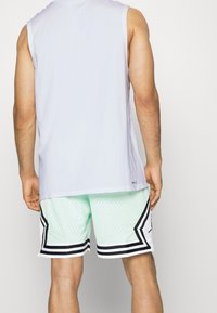 Ærmeløs lys lilla skjorte med rundet kant over mintgrønne mesh-shorts med sorte striber og et diamantmønster på siderne.