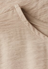 Svetle béžová tkanina s hladkým povrchem a jemnými vráskami. Má zaoblený výstřih a viditelné švy.