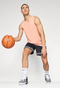 Rosa mesh tank top, svarte shorts med hvite striper, holder en oransje basketball. Skoene er svart og hvit med et mønstret design.
