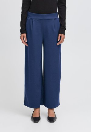 Navy wide-leg trousers made of a soft fabric with a smooth texture, featuring a high waistband and front pleats, paired with black shoes.
