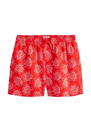 Nærbillede af en person iført lyserøde badeshorts med hvidt skildpaddemønster og elastisk linning med snøre.