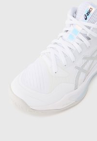 Λευκό αθλητικό παπούτσι κατασκευασμένο από πλέγμα και συνθετικά υλικά. Διαθέτει υφή στο επάνω μέρος, επίπεδα κορδόνια και ημιδιάφανο πάτο με σήμανση.