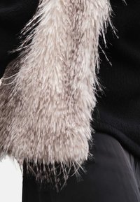 Faux fur in light beige with a textured, fluffy finish, contrasted against a dark black fabric background. Close-up view of the material.