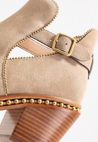Beżowe zamszowe buty na obcasie z złotym zapięciem, złotą koralikową obwódką wzdłuż krawędzi oraz z drewnianym, warstwowym obcasem.