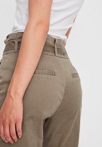 Pantalons en coton khaki avec taille haute, deux poches arrière et texture lisse. Portés avec un haut blanc ajusté.