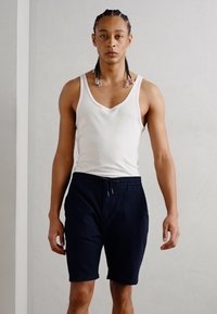 Top fără mâneci alb; pantaloni şort negri cu talie elastică şi șnur de ajustare; material neted, design ajustat, stil casual.