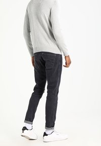 Grauer Pullover, schwarze Jeans, schlanker Schnitt, abgetragene Ärmel, weiße Sneakers und kontrastierende schwarze Akzente. Glatte Textur mit grundlegenden Design-Details.