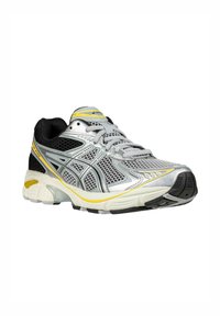 Zapatilla de correr en plata, negro y amarillo. Parte superior de malla con superposiciones texturizadas, lengüeta acolchada y suela blanca flexible para mayor soporte.