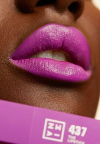 Rouge à lèvres violet appliqué sur les lèvres, avec une finition mate. L'emballage en dessous est d'un violet éclatant avec un texte blanc indiquant "437 Le Rouge à Lèvres."