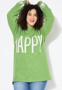Vihreä neulepaita, jossa on valkoiset kirjaimet "HAPPY" edessä, rento malli ja pitkät hihat, yhdistettynä sinisiin farkkuihin.