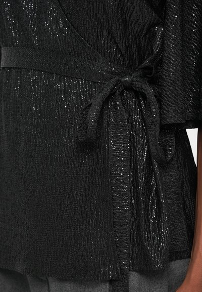 Haut noir texturé avec un lien à la taille, présentant un léger éclat et des manches amples, complétant un design fluide.