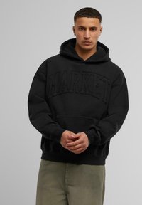 Schwarzer Kapuzenpullover mit dem Aufdruck "MARKET" auf der Vorderseite, Kängurutasche und verstellbarem Kordelzug an der Kapuze. Weicher Stoff und lockere Passform.