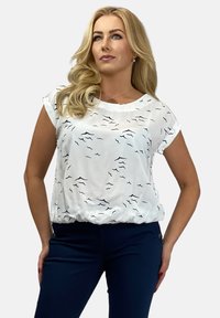Biała bluzka z czarnym wzorem w fale, z krótkimi rękawami i marszczonym dołem. Noszona z granatowymi spodniami, charakteryzującymi się gładką tkaniną i dopasowanym krojem.