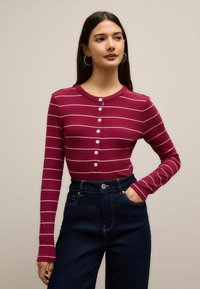 Mørkerød ribbeind hollawvnt trøje med hvide vandrette striber og knaplukninger, parret med mørke højtaljede denim jeans.