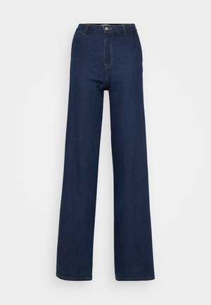 Jean en denim bleu foncé à jambe large et taille haute, avec une fermeture à bouton sur le devant, des coutures discrètes et une texture lisse et robuste.