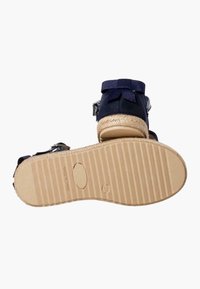 Navy fabric sandal with a woven espadrille sole and rubber outsole. Features a bow accent and adjustable buckle strap.
