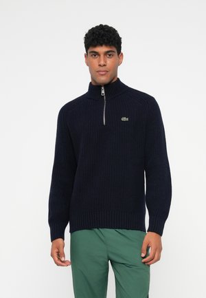 Maglione a collo alto di colore blu navy con mezza zip. Caratterizzato da polsini e orlo a coste, e un piccolo logo verde sul lato sinistro del petto.