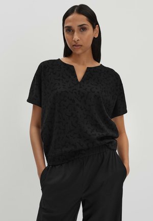 Top noir à manches courtes avec une texture subtile, présentant un décolleté en V et une coupe décontractée, associé à un pantalon noir à taille élastique.