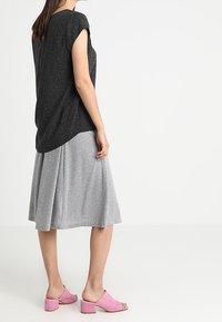Czarny top z krótkim rękawem o teksturowanym wykończeniu, zestawiony z szarą spódnicą w paski o kroju litery A i różowymi sandałami typu mule z odkrytymi palcami. Prosty fason i luźne dopasowanie.