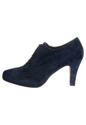 Granatowe zamszowe buty na wysokim obcasie z zamkniętym noskiem, ozdobnym detalem w stylu brogue i smukłym obcasem. Gładka faktura i elegancki kształt.